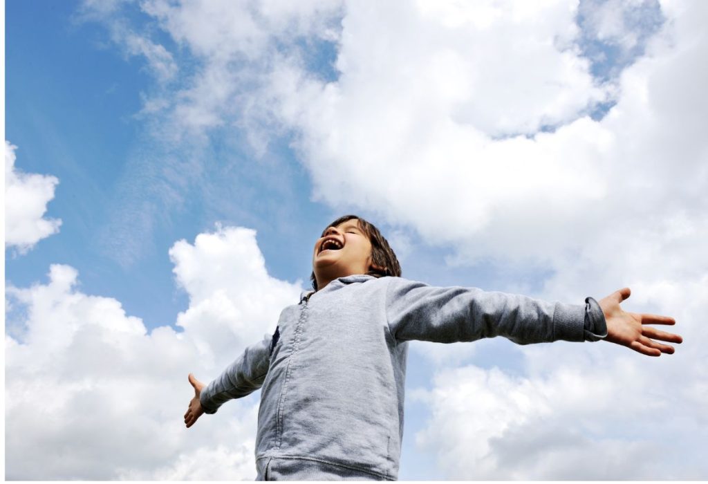 A child with arms spread wide inhaling deeply under a partly cloudy sky
