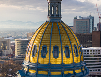 A midair shot of a golden domed building with a cityscape in the background.